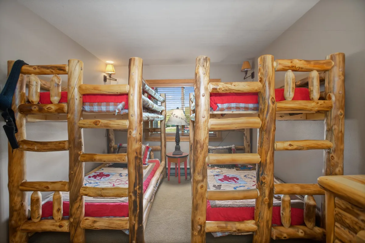 A playful bedroom with bunk beds, decorative quilts, a lamp, and a window offering natural light. The space is designed for groups or families, inviting cozy storytelling and shared adventures.