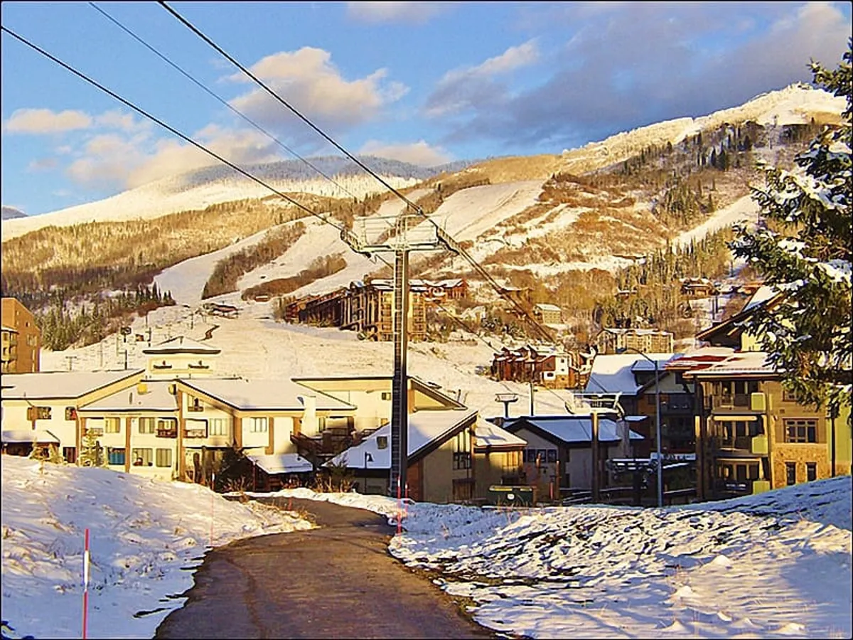 A vibrant winter scene featuring snow-covered mountains, a ski lift, and nearby residential buildings. A well-trodden pathway leads adventurers from the heart of the base area to the slopes, capturing the lively, active spirit of Gondola Square.