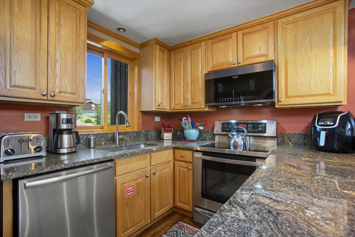 A functional kitchen environment with granite countertops, wooden cabinets, modern appliances, and a window view. The space feels ready for anything from morning coffee to festive family gatherings, blending practicality and warmth.