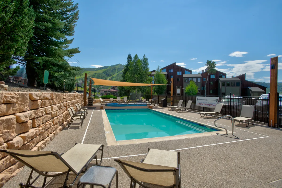 A sparkling swimming pool surrounded by lounge chairs, shaded seating, and a dramatic mountain backdrop. The scene is lively yet relaxing, ideal for families looking to unwind or make a splash after a day of adventure.