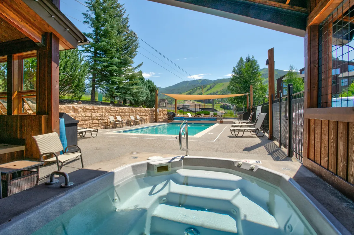 This inviting exterior scene showcases a sparkling swimming pool with a hot tub nearby, surrounded by lounge chairs and offering sweeping mountain views. The tranquil environment is accentuated by the sunset glow and relaxing resort vibe.
