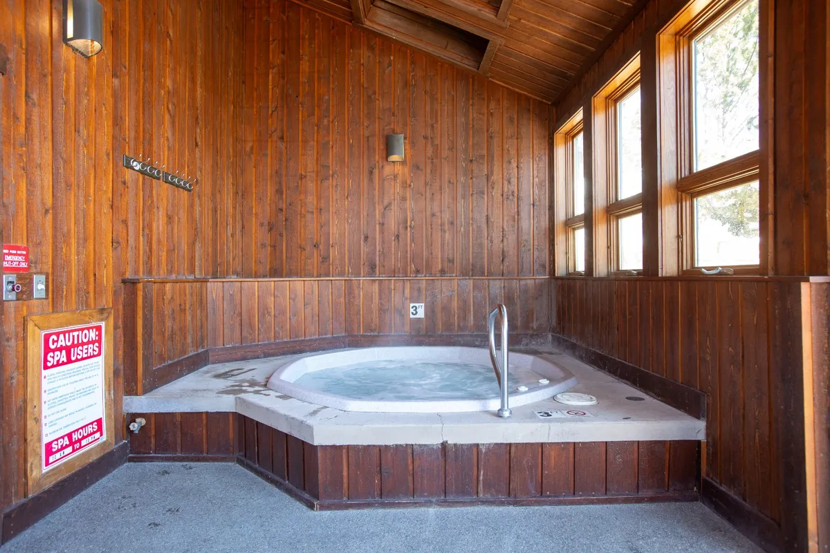 A cozy interior hot tub area with wooden walls and large windows, inviting guests to relax and socialize in a tranquil spa-like environment with natural light.
