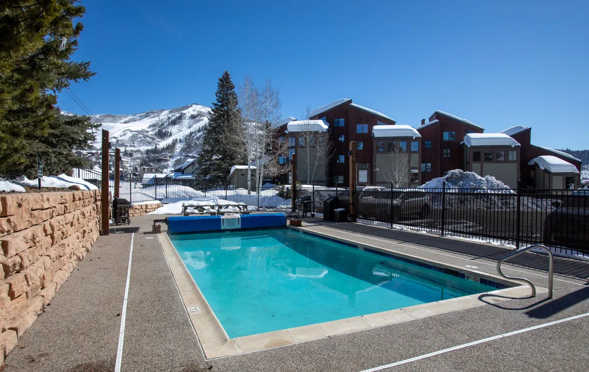 A pool scene surrounded by a snow-covered landscape, with mountains rising in the background and a fenced-in area creating a sense of privacy and exclusivity. The scene highlights the year-round appeal of the heated pool and outdoor relaxation, even in winter.